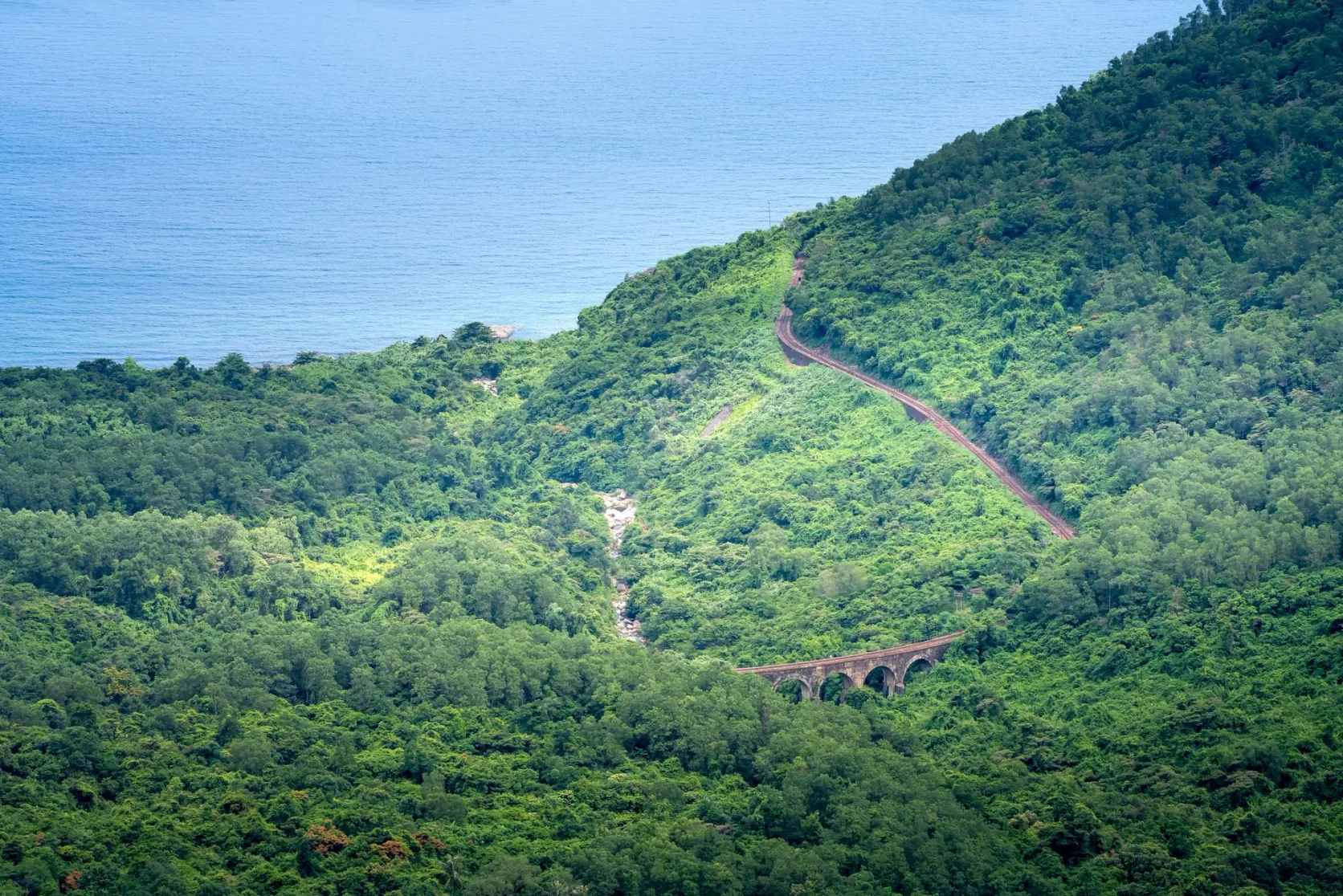 Die Bahnstrecke schwingt sich nahe dem Hải-Vân-Pass an einem bewaldeten Hang über dem Meer entlang.
