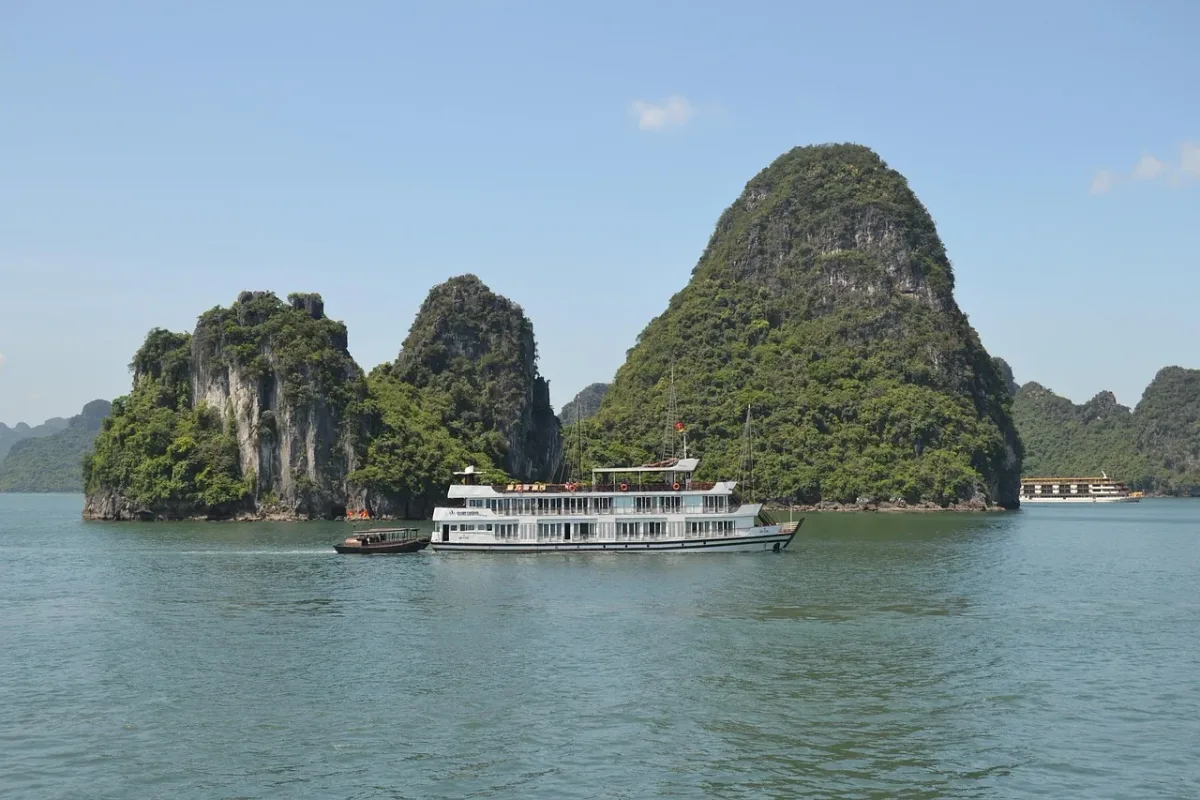 Ein Kreuzfahrtschiff fährt an hohen Kalksteinfelsen in der Halong-Bucht vorbei.