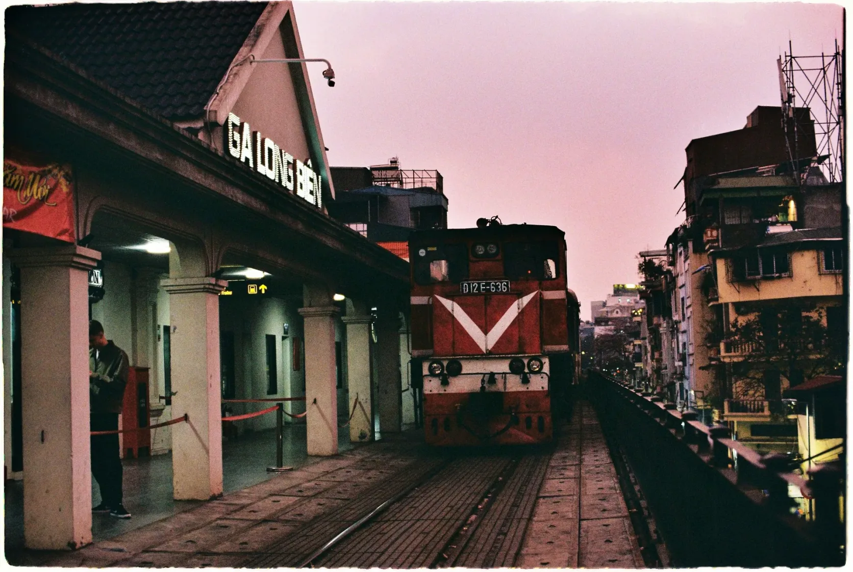 Eine rote Diesellok am Bahnhof Long Biên in Hanoi, unter dem Bahnhofsschild.