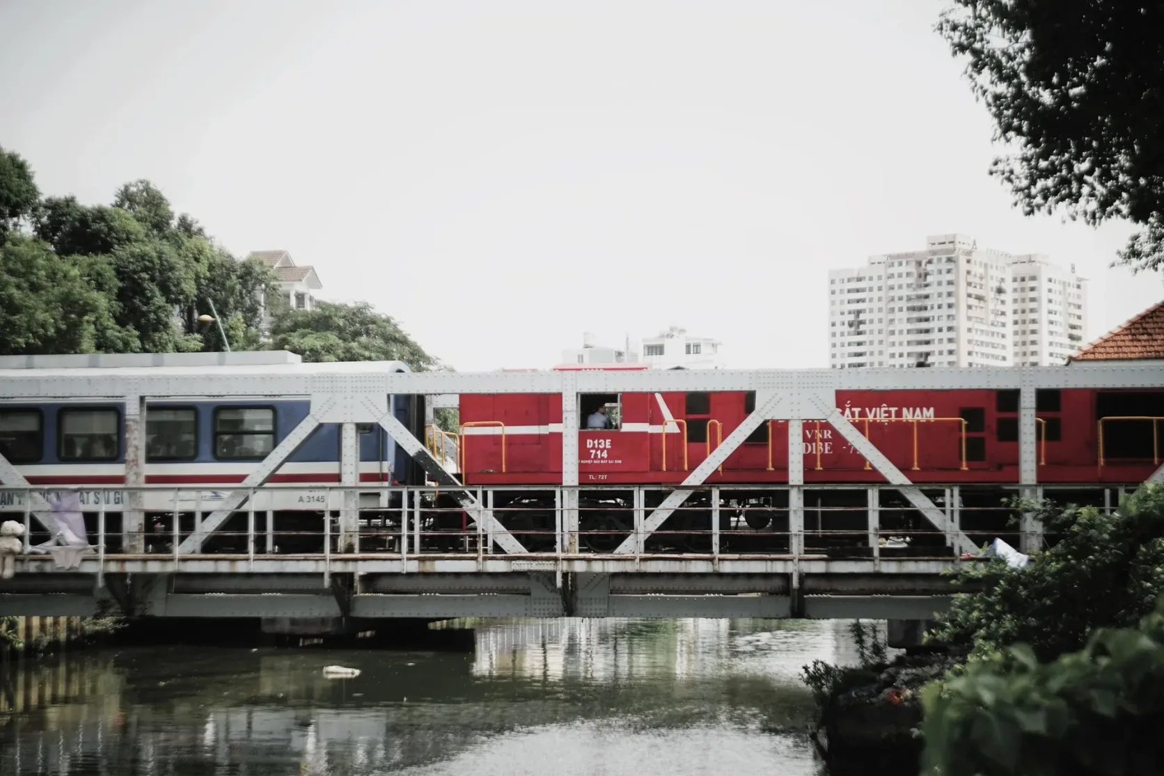 Ein Zug auf einer Brücke über einen Kanal, mit Stadtgebäuden im Hintergrund.