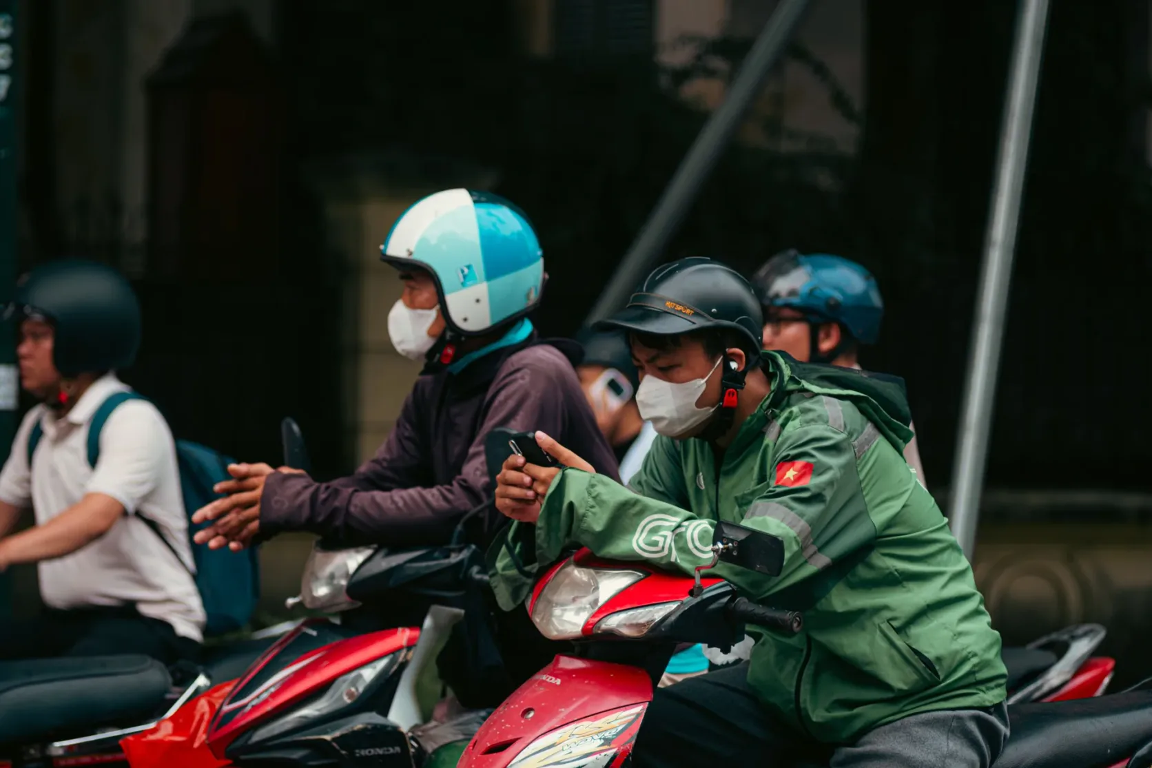 Ride-hailing riders in green jackets in traffic.