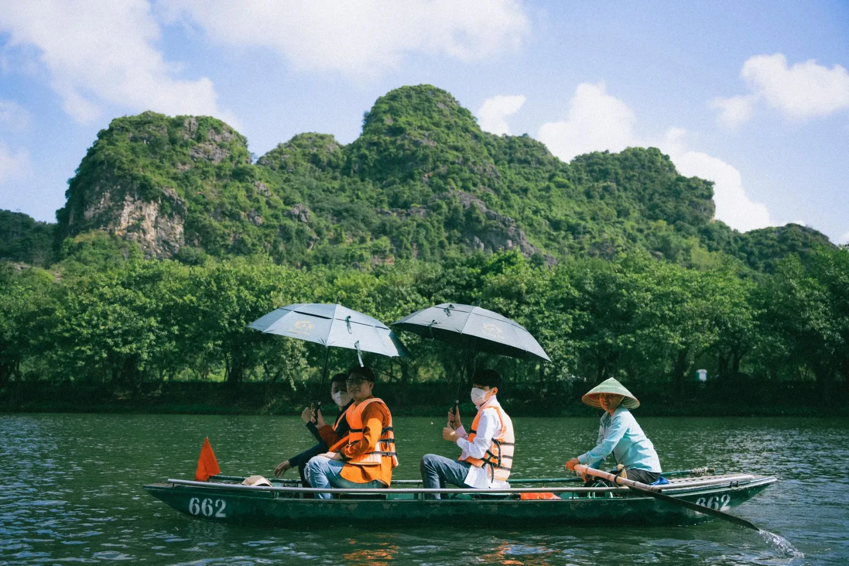 Una barca de remos con sombrillas bajo un peñón kárstico verde en Ninh Binh.