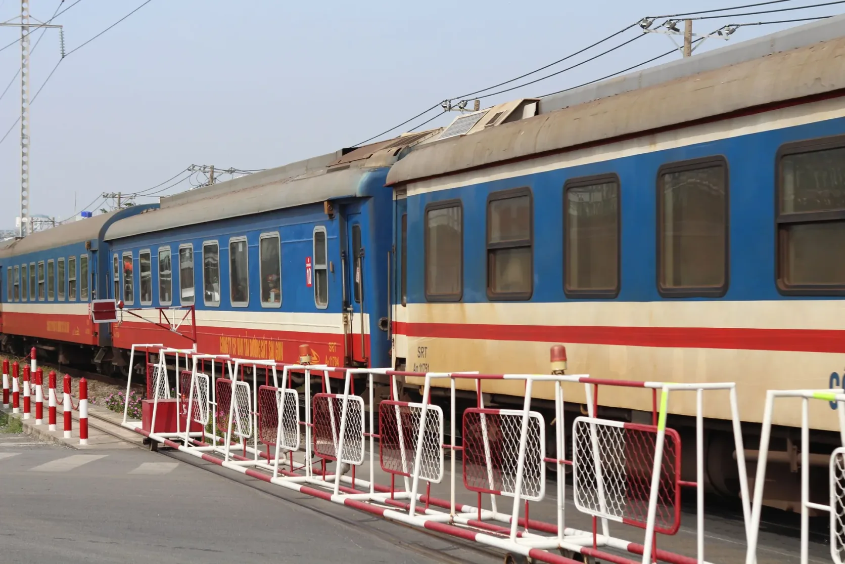 Vagones de pasajeros de un tren vietnamita pasando por un paso a nivel.